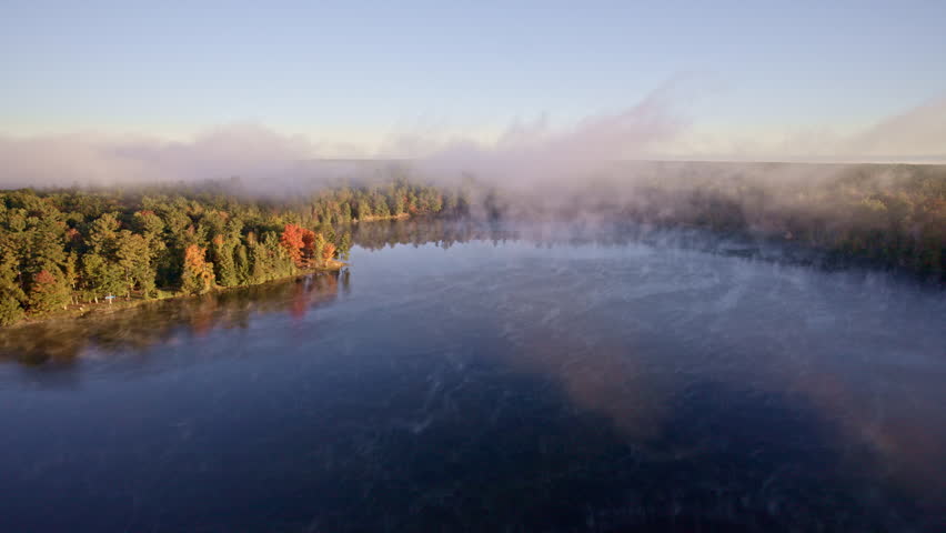 Cinematic overhead shot of dawn mist dispersing above the water.