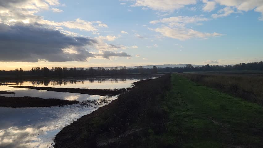 Serene 4K lake sunset with dramatic clouds and bright reflections near Vancouver Lake in Washington. Peaceful fall scenery with calm water and warm light, great for background, marketing presentations