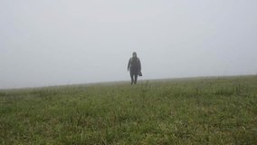 A man in a long coat walks across a grassy, empty field in the fog. Cold weather, alone. - Powered by Shutterstock - Get 15% off with code: PIKWIZARD15