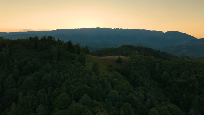 Moieciu–Bran, Transylvania — golden-hour panorama of rolling hay meadows and birch tree belts, rustic animal shelters, contrasted with the cool silhouette of the Piatra Craiului ridge, Romania
