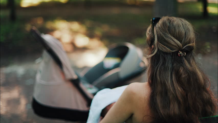 Close up of a stroller with a mother breastfeeding her baby while sitting on a park bench in the background