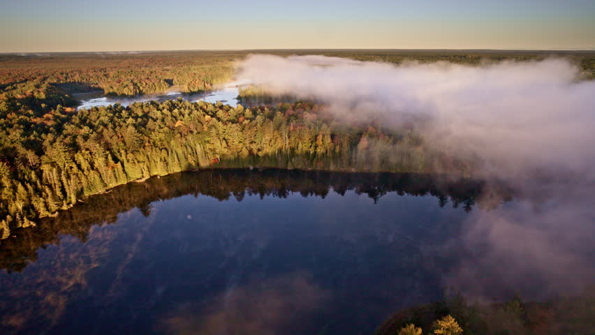 Cinematic drone view of mist drifting upward from the water at daybreak.