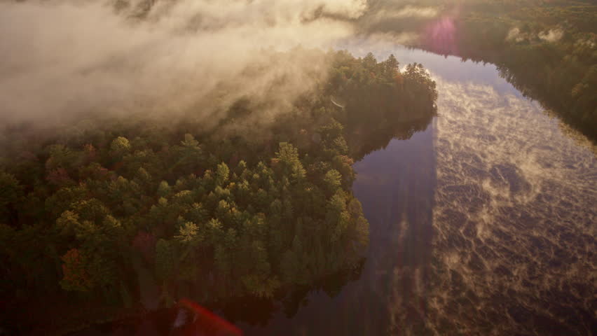 Aerial cinematic pass over water with mist glowing in dawn light.