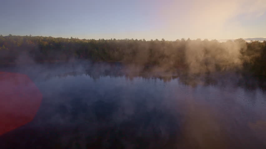 Drone captures gentle mist lifting over water at early sunrise.
