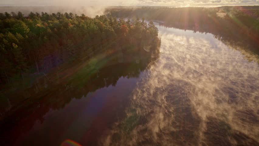 Aerial footage of mist drifting upward as the sun rises over water.