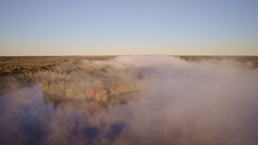 Drone passes over water as mist ascends in the early morning light.