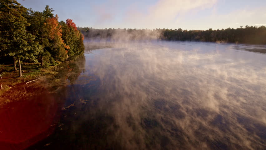 Aerial perspective of mist drifting up from water in dawn glow.