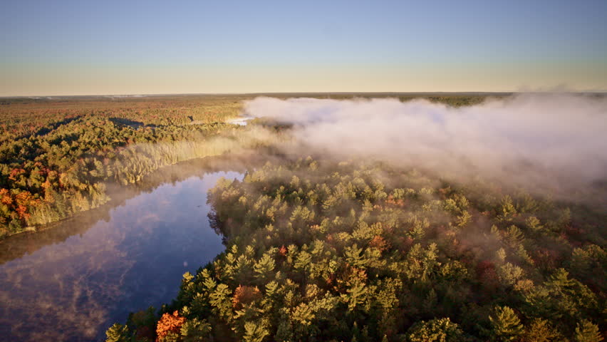 Aerial shot showing mist lifting over water during sunrise.