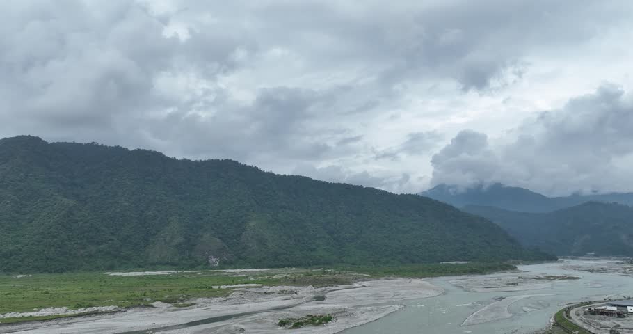 Drone view of misty mountains and a winding river under heavy clouds. Moody, cinematic landscape scenery.