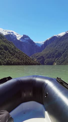 A vertical first-person perspective of a boat front during the sail in tranquil waters with snowy peak at Queulat National Park in Aysen region, Chile