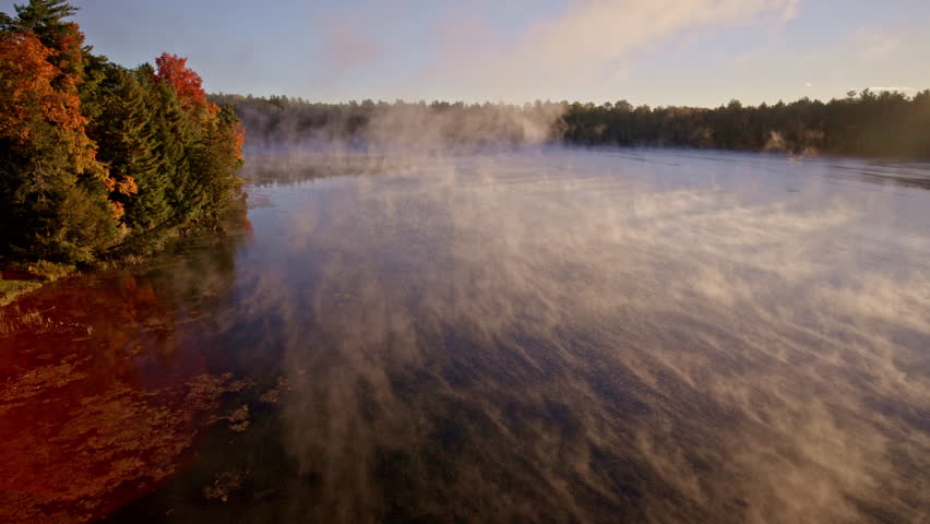 Cinematic aerial view of dawn mist hovering and rising over water.