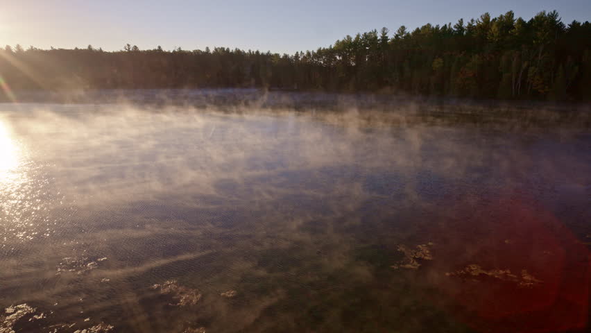 Drone view of rising morning haze over still water.