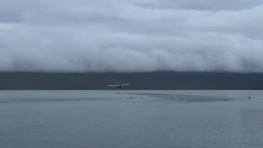 A Seaplane flying in dramatic sky with low clouds above Naknek Lake and another one standing on water, it