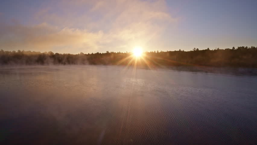 Cinematic drone shot of mist rising over water at dawn.