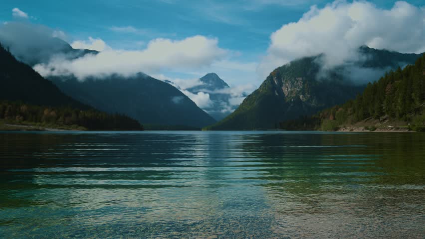 Plansee lake, alps mountains and autumn trees mirrored in calm blue clear water under blue sky. Austria