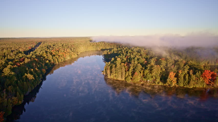 Cinematic drone view of early morning mist drifting upward over water.