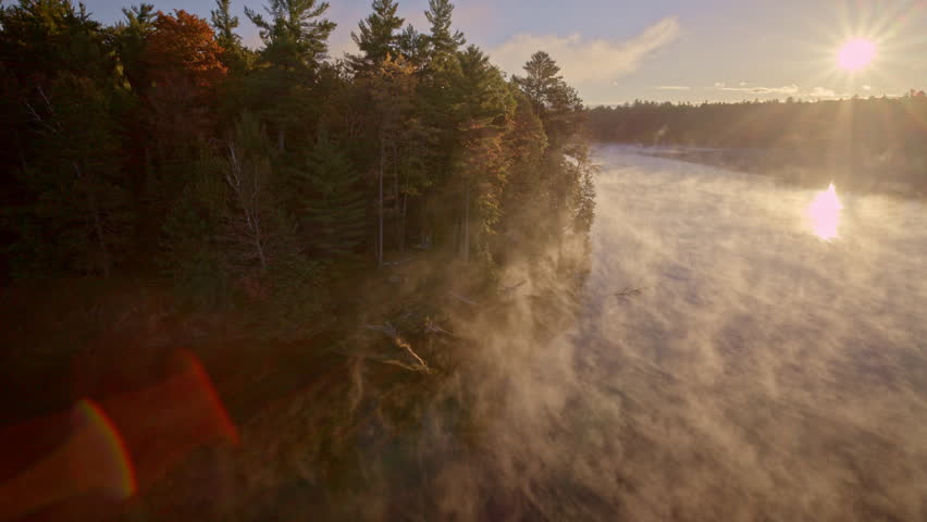 Cinematic aerial angle of mist drifting off water at sunrise.