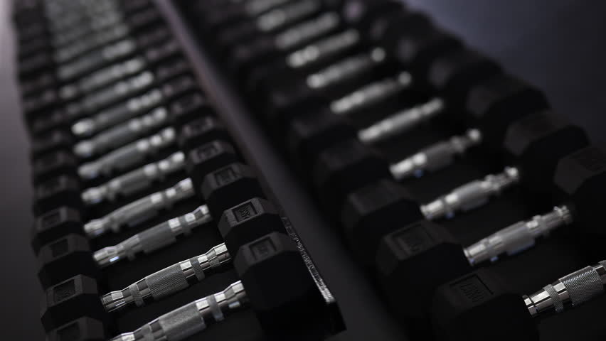 A young woman in a modern gym taking dumbbells from an organized rack before starting her workout. Stylish fitness environment with clean equipment, showcasing strength training and active lifestyle.