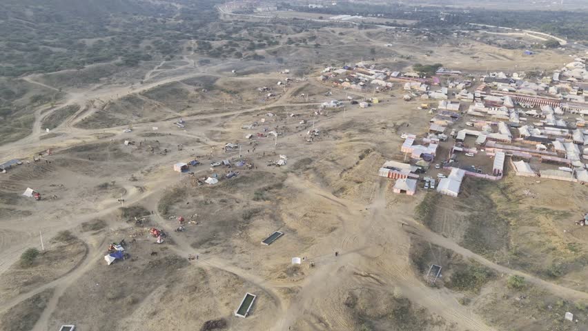 Aerial shot of camels and horse tents at Pushkar cattle fair ground, with Aravalli mountains in the background under soft morning light.