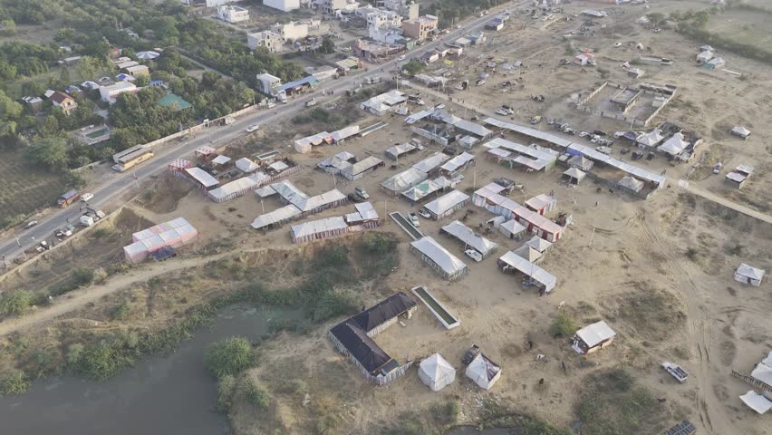 Aerial shot of a pond near Pushkar cattle fair ground with horse tents, captured at sunrise with Aravalli mountains in the background.
