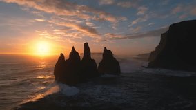 Aerial view of basalt sea stacks at Reynisfjara beach, silhouetted against a vibrant sunset sky, with waves crashing around them, Reynisfjara, Myrdalshreppur, Iceland. - Powered by Shutterstock - Get 15% off with code: PIKWIZARD15