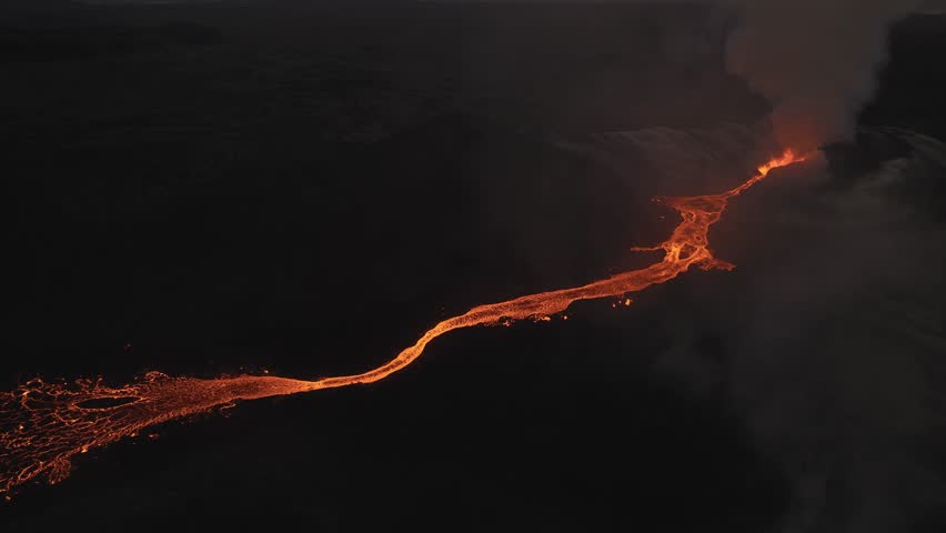 Aerial view of a river of fiery orange lava snaking through a dark, barren landscape, contrasting with the smoky plumes rising above, Grindavikurbaer, Iceland.