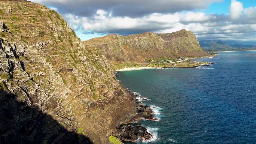 Aerial view of rugged coastline meeting the deep blue ocean, contrasted against the backdrop of majestic mountains, Makapu