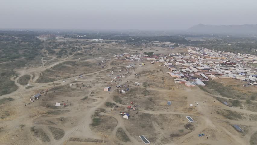 Aerial shot of the Pushkar cattle fair ground in Rajasthan, featuring camel and horse tents spread across the desert landscape with the Aravalli mountains in the background.