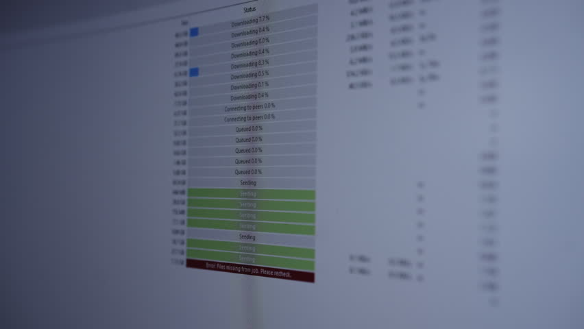 Closeup of computer screen showing torrent client application with file download and upload statuses, including progress bars and noticeable error message about missing files, slow motion.