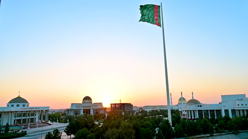 Turkmen flag waving over the center of Mary, Turkmenistan at sunrise