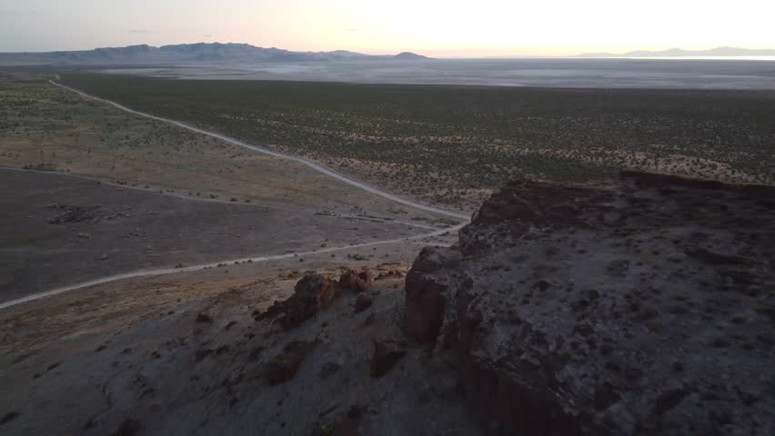 Drone clip of a long dirt road through barren Utah desert land with subtle sunset colors and distant rock formations creating a scenic and atmospheric view.