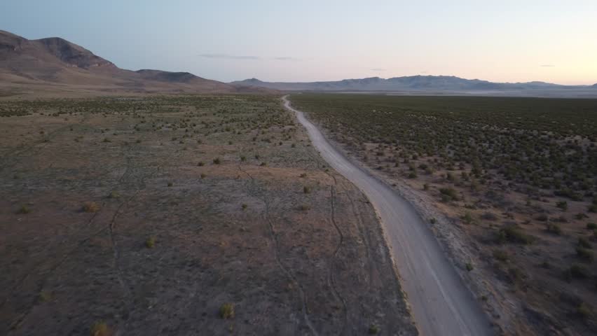 Aerial pass over a dusty desert track toward canyon ridges during sunset, highlighting Utah’s rugged landscape and offering strong cinematic visuals.