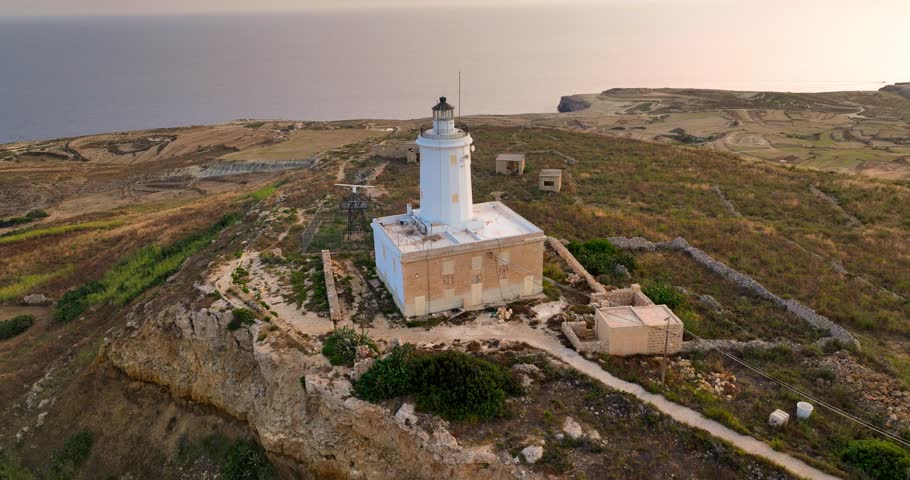 Aerial view of Ta' Gurdan Lighthouse standing tall on the rugged coastline, contrasting sharply with the tranquil blue sea, Ghasr, Gozo, Malta.