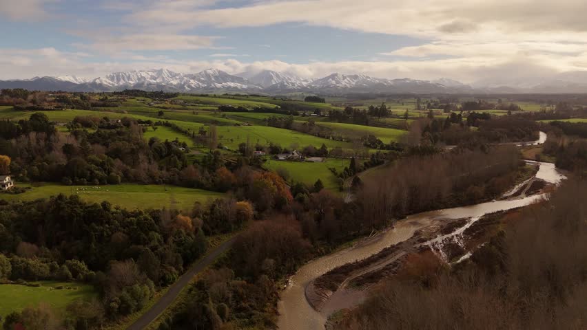 Green hills with withered trees by the river with snowy mountains during autumn, aerial shot