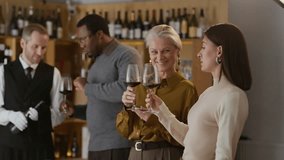 Medium shot of elegant Caucasian women engaged in conversation at wine tasting event with young Black man talking to middle-aged Caucasian sommelier working in fine dining restaurant - Powered by Shutterstock - Get 15% off with code: PIKWIZARD15
