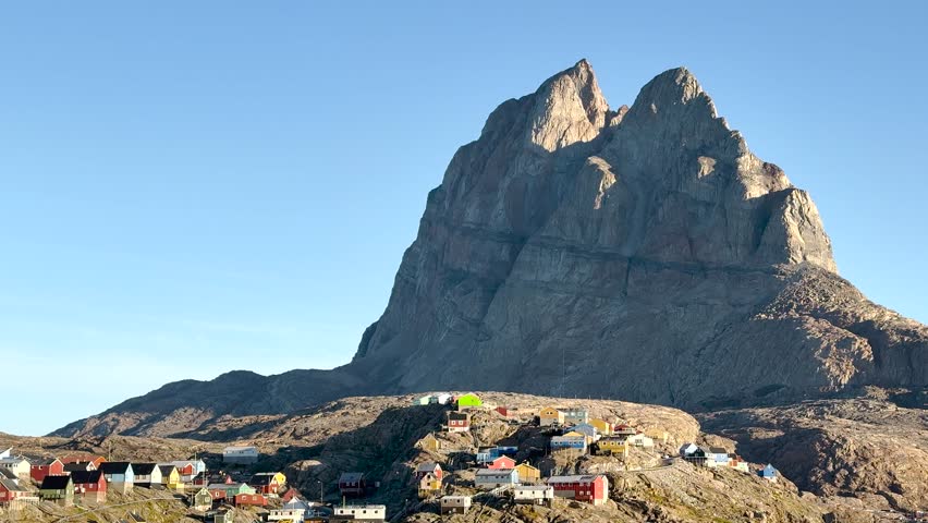 Explore a vibrant settlement on the coast of Greenland, featuring colorful houses against a backdrop of rocky hills and calm waters. This picturesque location offers stunning views.