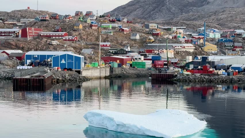 Explore a vibrant settlement on the coast of Greenland, featuring colorful houses against a backdrop of rocky hills and calm waters. This picturesque location offers stunning views.