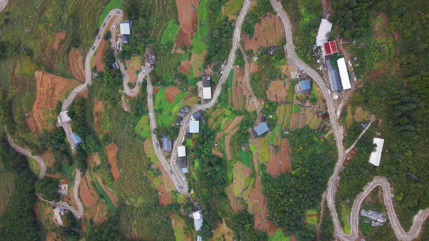 Aerial top-down view of winding serpentine roads cutting through the hills of Wuxi County, Lingpaishi, revealing zigzag paths, scattered homes, farmland patches and lush mountainous terrain. UHD.