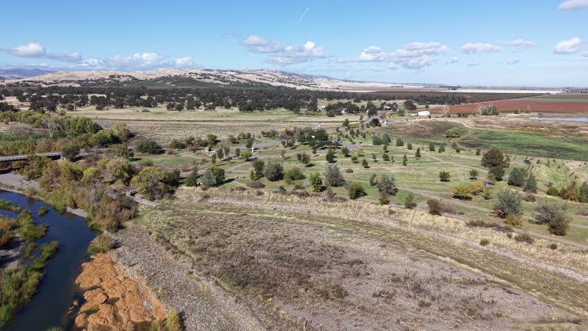 Drone footage moving laterally from left to right over Capay Valley in California, showing Cache Creek, dry vegetation, farmlands, and distant hills under a clear sky.