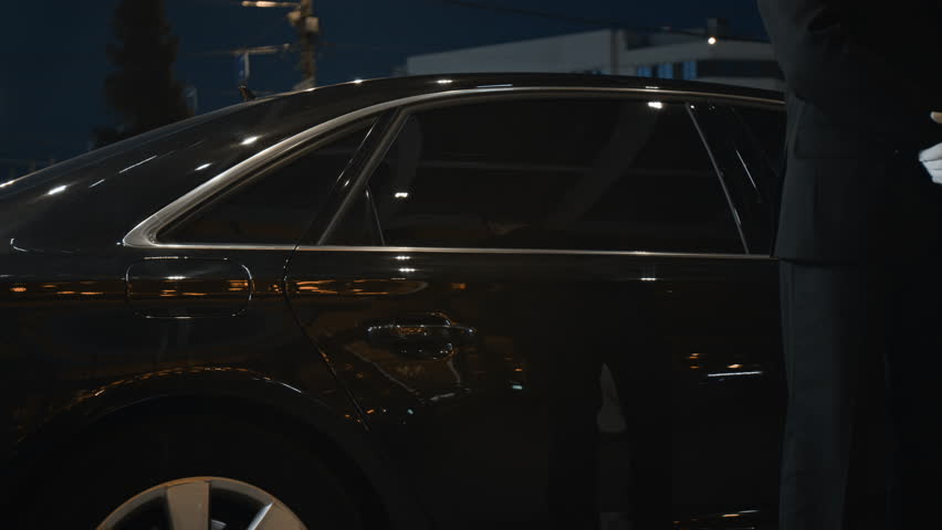 Cropped shot of professional personal driver in white gloves opening car door for female VIP passenger assisting client during departure in evening
