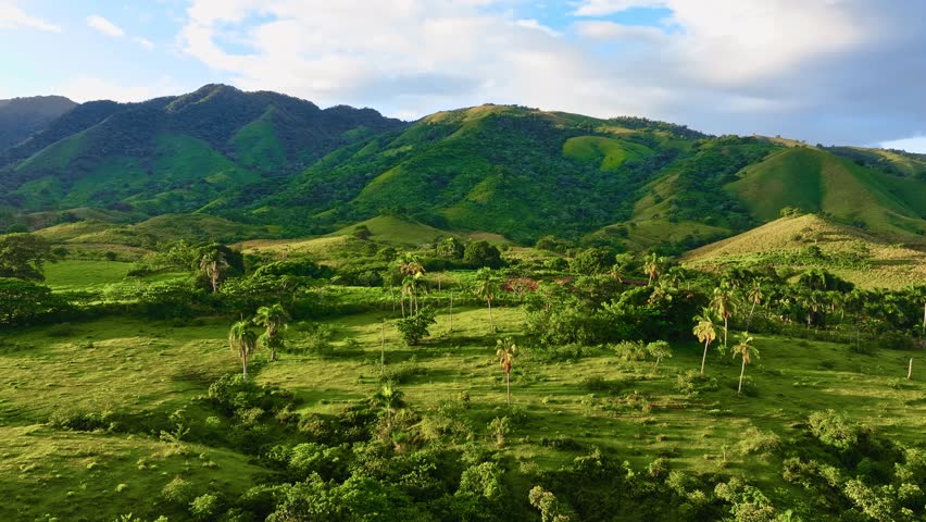 A beautiful panoramic view of a sun-drenched mountain range. Forested foothills under a cloudy sky. A stunning aerial view of a tropical mountain landscape with lush pastures. Dominican Republic.