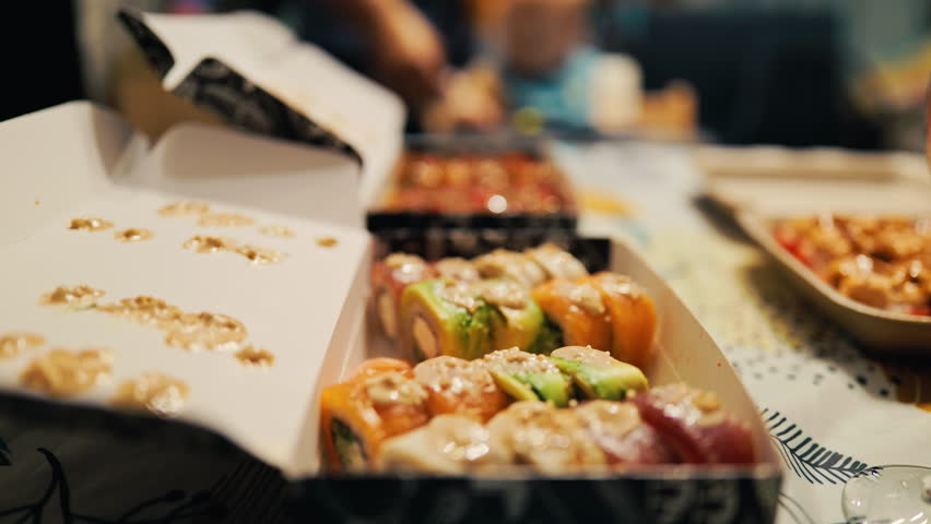 Mixed sushi pieces and nigiri displayed in open box on patterned cloth during work break or social