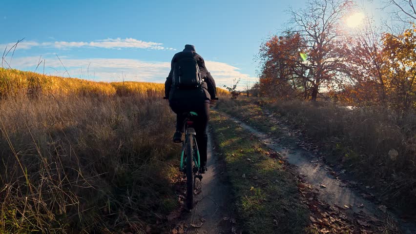 A female cyclist rides along a field and a river on an autumn day