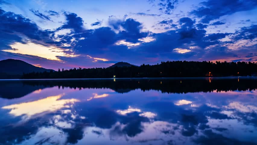 Beautiful time-lapse of Mirror Lake in Lake Placid, New York, capturing calm water, drifting clouds, surrounding mountains, and the peaceful atmosphere of a scenic summer day in nature.