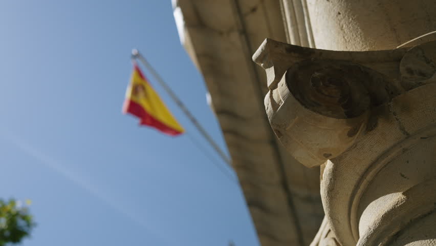 Spanish Flag Waving Beside Historic Stone Column