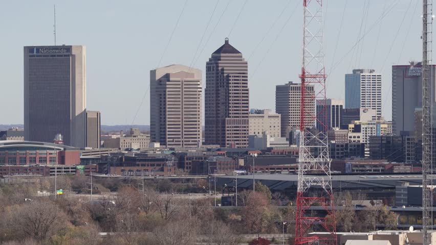 Helicopter aerial establishing shot of Columbus, Ohio capital city with big business towers, arena district, highway car traffic, and warm autumn fall tree leaves with multiple downtown businesses