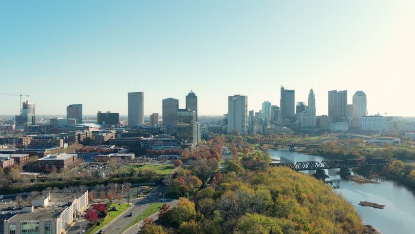 Helicopter aerial establishing shot of Columbus, Ohio capital city with big business towers, arena district, highway car traffic, and warm autumn fall tree leaves with multiple downtown businesses