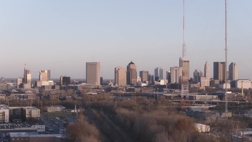 Helicopter aerial establishing shot of Columbus, Ohio capital city with big business towers, arena district, highway car traffic, and warm autumn fall tree leaves with multiple downtown businesses