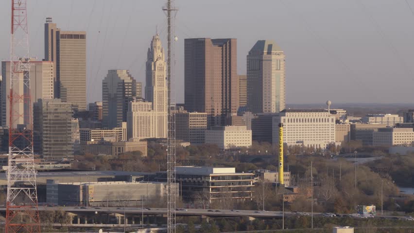 Helicopter aerial establishing shot of Columbus, Ohio capital city with big business towers, arena district, highway car traffic, and warm autumn fall tree leaves with multiple downtown businesses