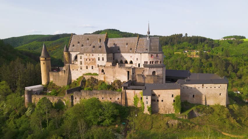 vianden castle chateau de historical site green hills cloudy sky beautiful town homes cars parked upper area to reveals left near right circling drone shot luxembourg